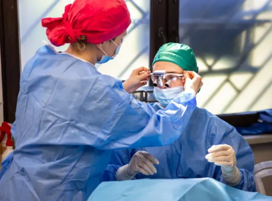 dwoje lekarzy przy operacji, jeden poprawia drugiemu okulary